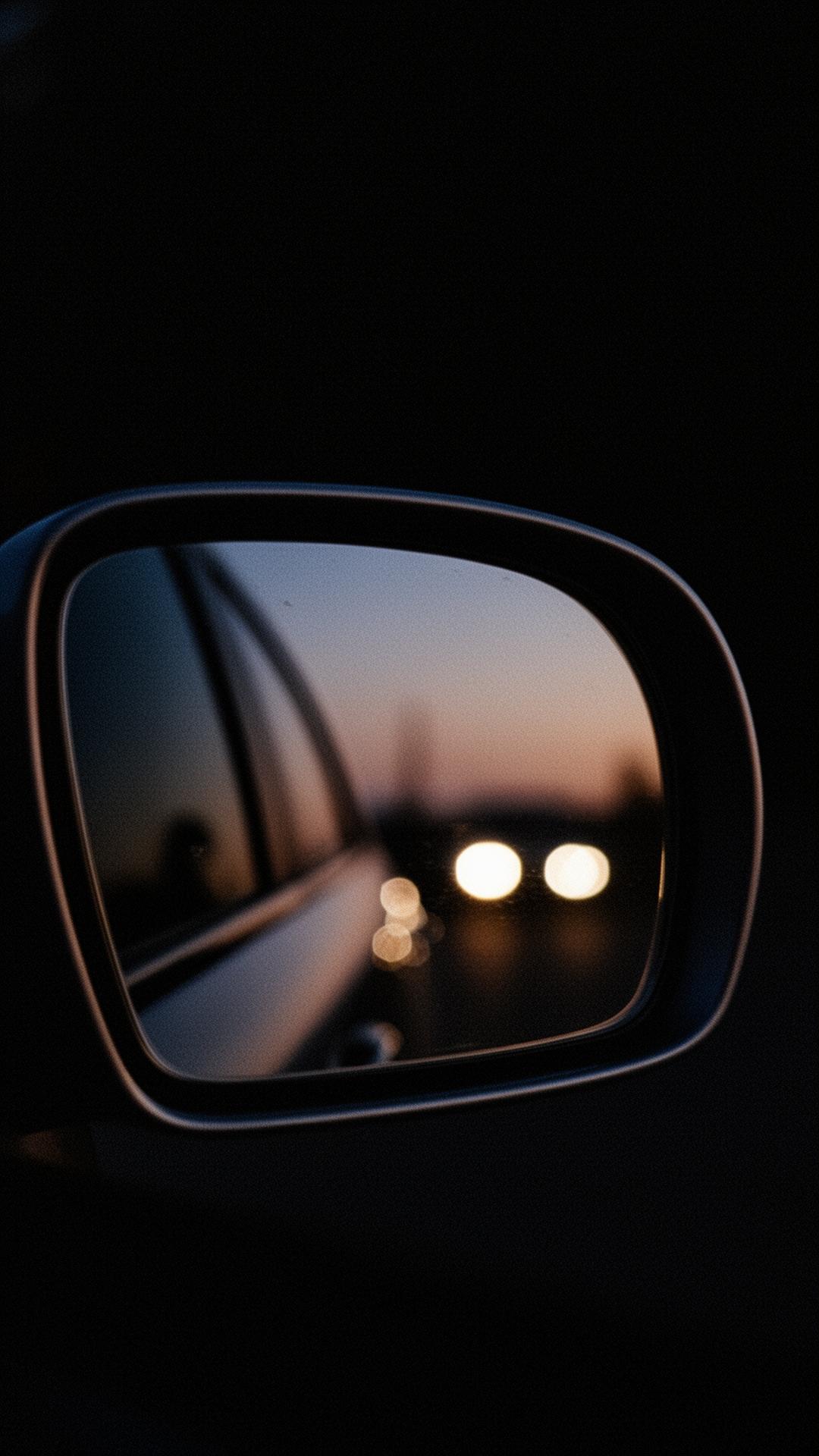 A side mirror at dusk reflecting distant headlights